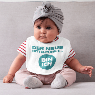 Ein Baby mit einem Body mit dem Druck "Der neue Mittelpunkt bin ich"