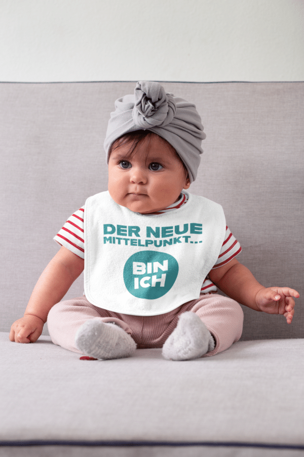 Ein Baby mit einem Body mit dem Druck "Der neue Mittelpunkt bin ich"